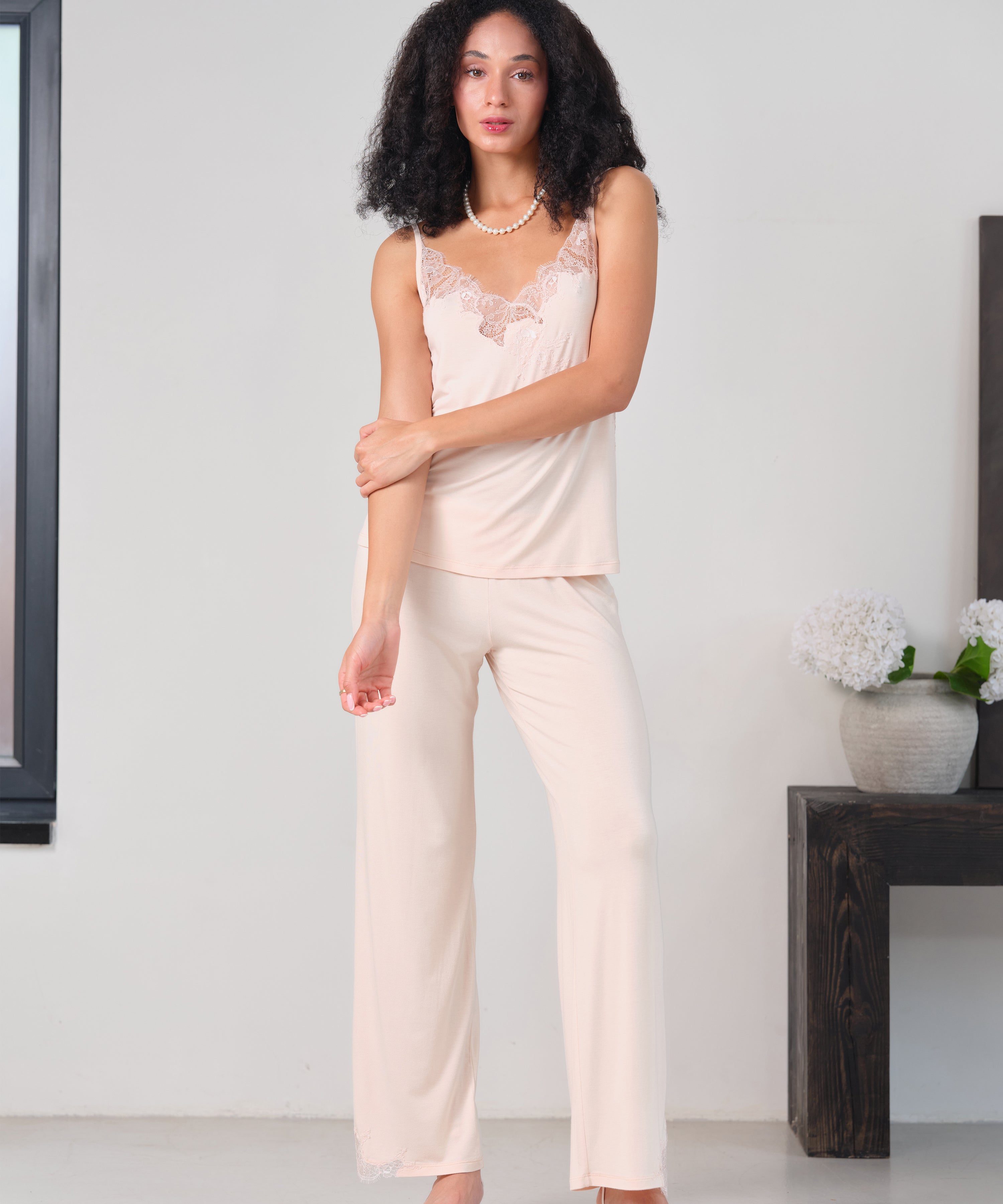 Effetto bamboo camisole pajama set 03163 – women's sleepwear, rosy peach
Woman wearing a light pink lace top and cream pants in a minimalistic room.