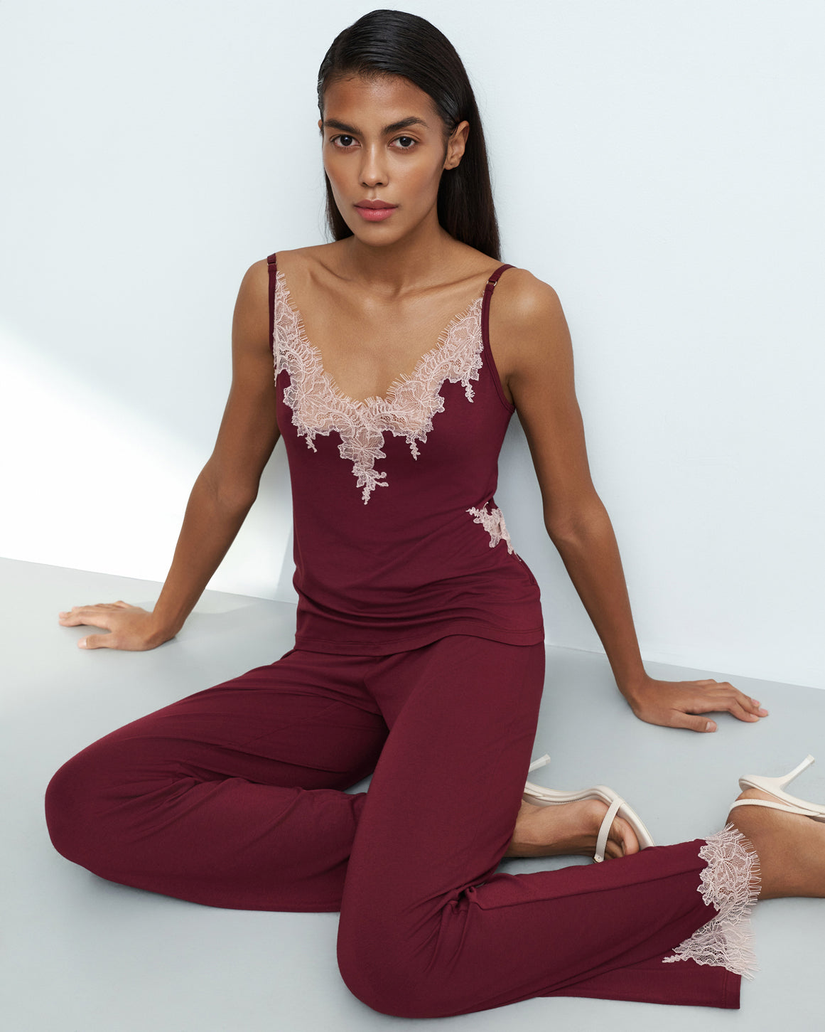 Effetto bamboo camisole pajama set 03163 – women's sleepwear, cherry lacquer
Woman wearing a burgundy jumpsuit with lace details sitting on a light gray surface.